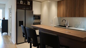 A modern kitchen with a central island, black chairs, a refrigerator, oven, microwave, and wooden cabinets. - Lovely apartment for 6 people with WIFI, pool, TV, balcony and panoramic view (Le Petit-saconnex)