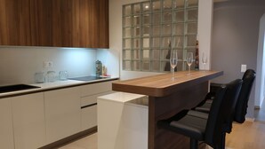A modern kitchen with a wooden countertop, a built-in sink, and a glass backsplash. There are three bar stools and a white refrigerator. - Lovely apartment for 6 people with WIFI, pool, TV, balcony and panoramic view (Le Petit-saconnex)