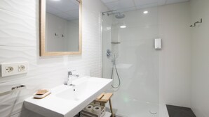Un baño moderno con lavamanos blanco, espejo y ducha con mampara de vidrio.