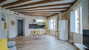 Amplia sala de estar con techo de madera, una mesa de comedor con sillas, un sofá con un cojín amarillo y un televisor sobre un mueble.