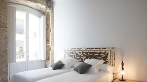 A room with two beds, a rustic brick wall, a white door, and a nightstand with a lamp. - PPRINCIPAL B - P B - APARTAMENTOS ALMADA - Plaza del Pilar (Zaragoza)