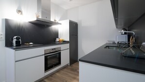 A modern kitchen with white cabinetry, a black countertop, a built-in oven, a stainless steel refrigerator, and a range hood. - PRIMERO B - 1 B - APARTAMENTOS ALMADA - Plaza del Pilar (Zaragoza)