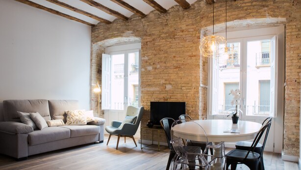 A living room with a sofa, chairs, a dining table, a TV, and a brick wall. - PRIMERO B - 1 B - APARTAMENTOS ALMADA - Plaza del Pilar (Zaragoza)