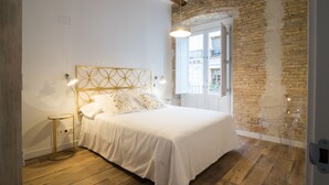 A bedroom with a white bed, a gold-framed headboard, a round bedside table, and a clear chair. - PRIMERO B - 1 B - APARTAMENTOS ALMADA - Plaza del Pilar (Zaragoza)