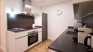 A modern kitchen with white cabinetry, a stainless steel range hood, a built-in oven, a refrigerator, and a coffee maker.