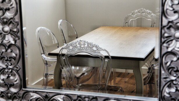 A dining table with chairs and a mirror with ornate frame.