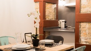 A dining area with a wooden table set for two, a potted plant, and a coffee machine. - PPRINCIPAL D - PD - APARTAMENTOS ALMADA - Plaza del Pilar (Zaragoza)