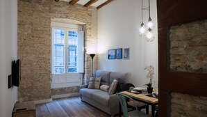 A cozy living room with a wooden floor, a grey sofa, a wooden table, and a window with a view of buildings. - PPRINCIPAL D - PD - APARTAMENTOS ALMADA - Plaza del Pilar (Zaragoza)