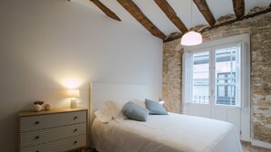 A bedroom with a bed, a dresser, a lamp, and a window with a view of buildings. - SEGUNDO D - 2D - APARTAMENTOS ALMADA - Plaza del Pilar (Zaragoza)