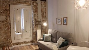 A cozy living room with a brick wall, a white door, a sofa with patterned cushions, and a hanging light fixture. - SEGUNDO D - 2D - APARTAMENTOS ALMADA - Plaza del Pilar (Zaragoza)