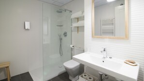A modern bathroom with a glass-enclosed shower, a white toilet, a white sink with a mirror, and a wooden shelf. - SEGUNDO D - 2D - APARTAMENTOS ALMADA - Plaza del Pilar (Zaragoza)