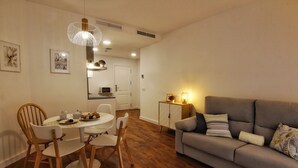 A modern living room with a grey sofa, wooden chairs, a dining table, and a kitchen in the background. - ENTRESUELO A - E A - Apartamentos Almada - Plaza del Pilar (Zaragoza)