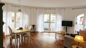 Amplia sala de estar con piso de madera, comedor con mesa y sillas, un sofá, una lámpara y un televisor.