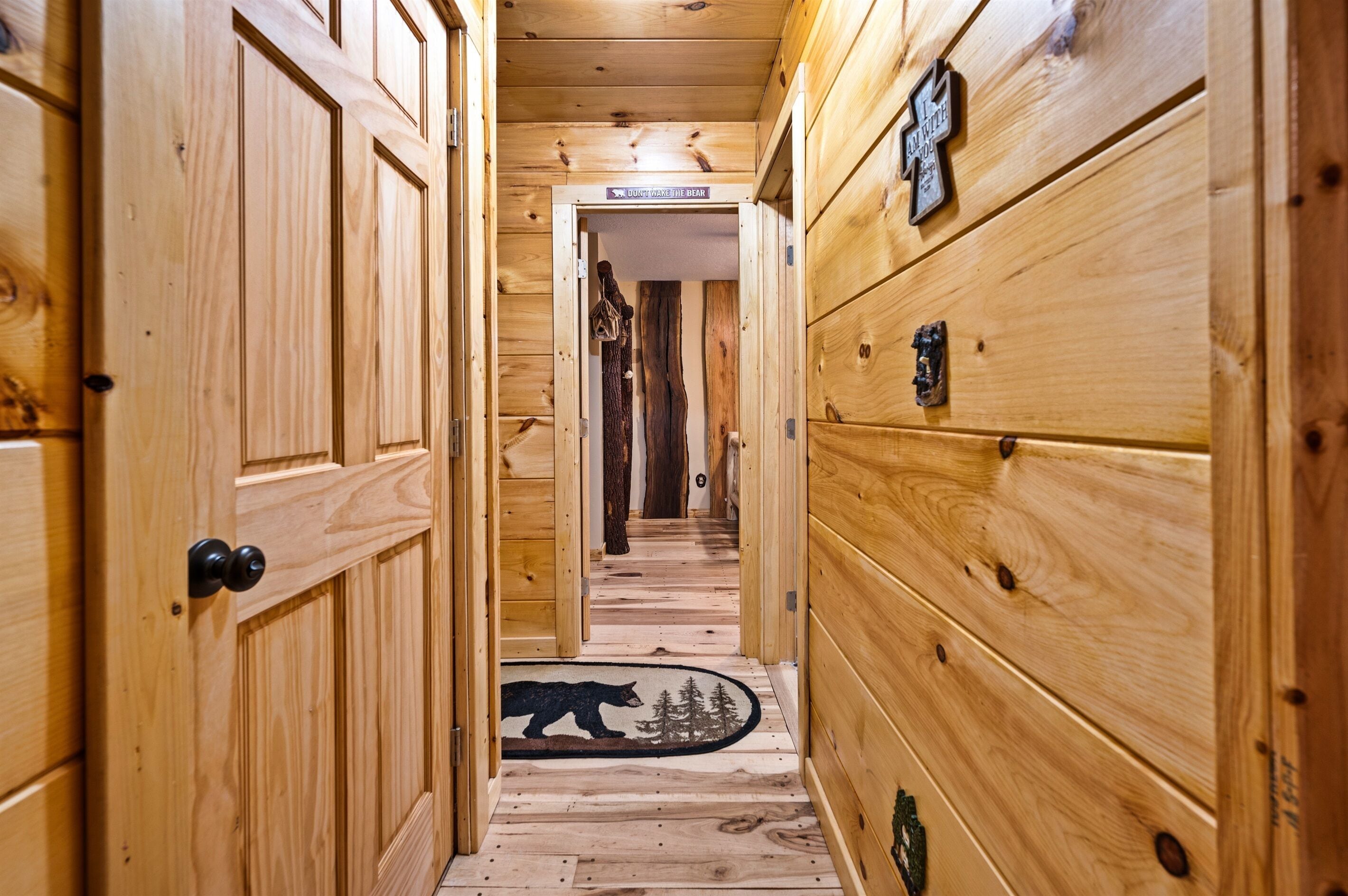 A wooden hallway with a bear rug at the end, wooden walls, and a sign that reads "Want to wake the bear?"
