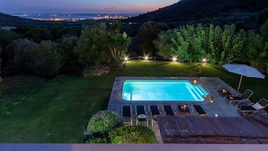 Une piscine rectangulaire à l’eau d’un bleu limpide, entourée d’une pelouse bien entretenue et de divers arbres.