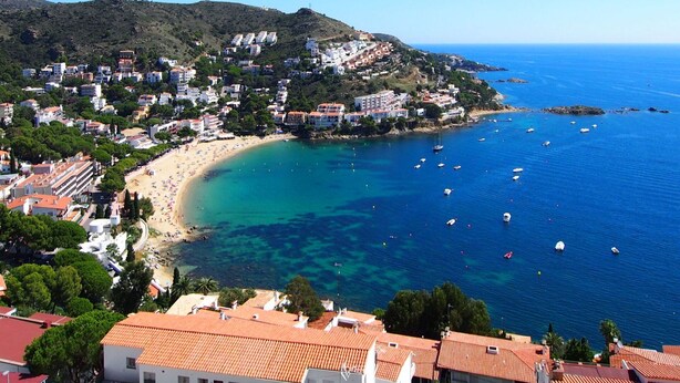 Une ville côtière dotée d’une plage, d’eaux d’un bleu limpide et de bâtiments aux toits recouverts de tuiles rouges.