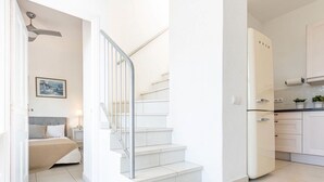 Un intérieur moderne et épuré, de couleur blanche, avec un escalier menant à une chambre et à un espace cuisine.