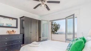 Une chambre à coucher comprenant un lit, une commode, une armoire, un ventilateur de plafond et un balcon avec vue.