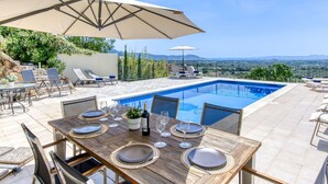 A poolside dining area with a table set for four, overlooking a swimming pool and a scenic view.