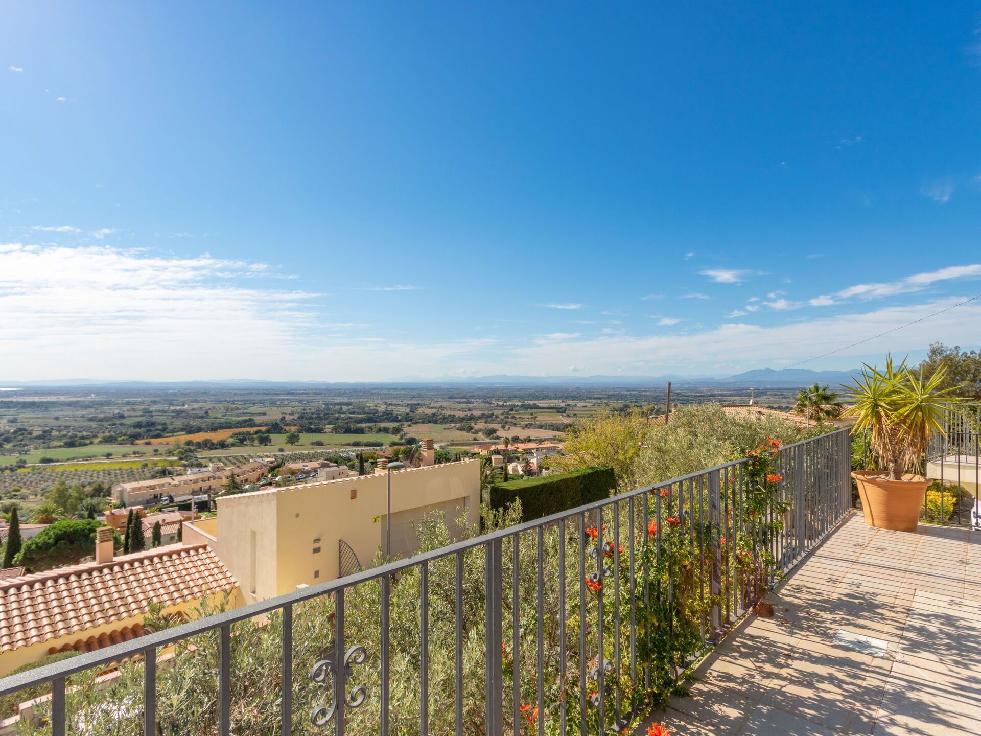 Ein Balkon mit Metallgeländer, der einen weiten Blick auf eine schöne Landschaft mit entfernten Gebäuden und Feldern bietet.