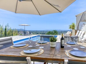 Une table en bois, dressée pour le repas, avec une piscine et une vue panoramique en arrière-plan.