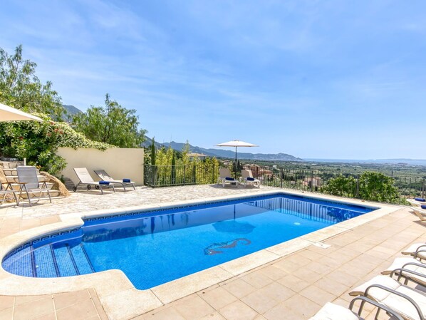 Une piscine dotée de chaises longues et d’un parasol, entourée de verdure et offrant une vue pittoresque.