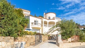 A Mediterranean-style villa with a stone facade, a curved balcony, and a stone staircase leading to the entrance.