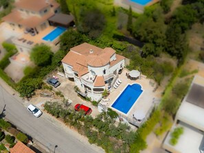 Une vue aérienne d’une grande maison dotée d’une piscine, de plusieurs voitures et d’une végétation luxuriante.