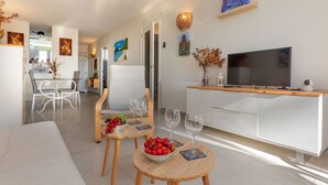 Een moderne woonkamer met een bank, twee eettafels, een televisie en een keuken op de achtergrond.