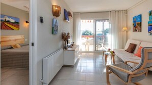 Een moderne woonkamer met een bank, een houten stoel, een eettafel en uitzicht door een glazen deur op een terras.