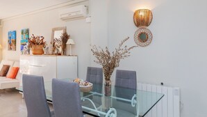 Een moderne woonkamer met een glazen eettafel, grijze stoelen, een witte bank en decoratieve wandkunst.
