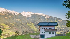 Ein modernes, zweistöckiges Gebäude mit Flachdach, gelegen auf einem grasbewachsen Hügel vor einer Bergkulisse.