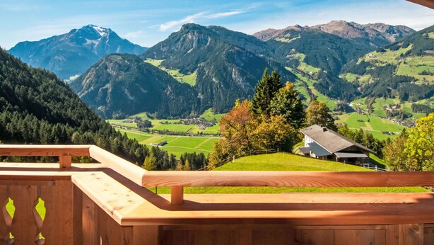 Ein Holzbalkon mit Blick auf eine gebirgige Landschaft, darunter grüne Felder und ein Haus.