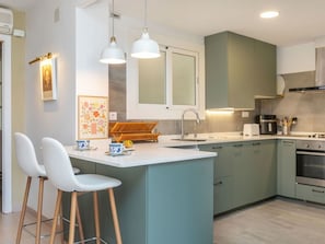 A modern kitchen with a central island, bar stools, a sink, and a stove.