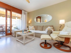 A hotel room with a sofa, a small table with a glass, a chair, a round wooden stool, a mirror, and a balcony with a view.