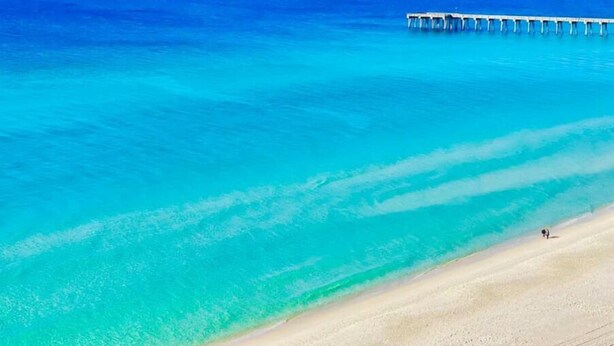 A beach with clear turquoise water and a wooden pier extending into the sea. - Surfside Serenity at Bidawee PCB (Panama City Beach)