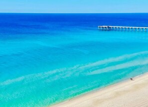 Une plage à l’eau turquoise et limpide, avec une jetée en bois qui s’avance dans la mer.