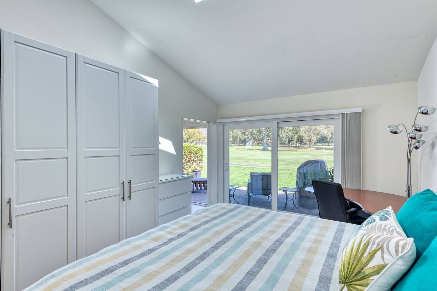 A bedroom with a large bed, a sliding glass door leading to a patio with outdoor furniture.