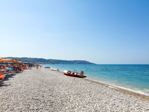 Una playa de guijarros con sombrillas y barcos.