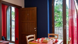 Une pièce avec une porte en bois portant le numéro 3, une table rouge avec une chaise blanche, et une vue sur la verdure à l’extérieur.