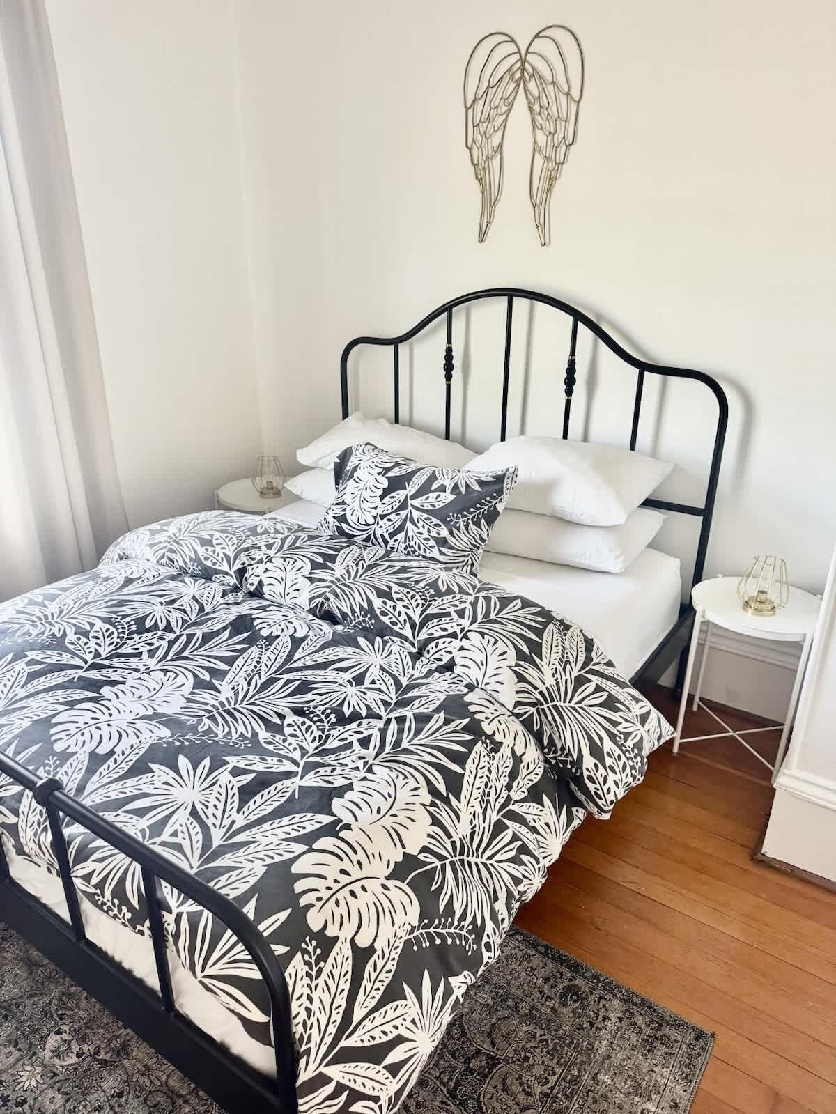 A bed with a black and white floral bedspread, a white pillow, and a black metal headboard.