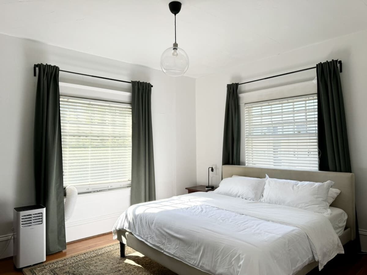 A bedroom with a bed, two bedside tables, a nightstand, a ceiling light, and a window with curtains.