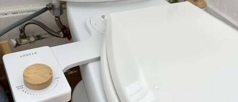 Des toilettes avec une poignée de chasse d’eau en bois et un tuyau apparent.