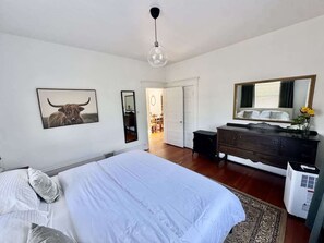 A bedroom with a large bed, a dresser, a mirror, and a door leading to another room. - *KING BED* Charming 2 bdrm above Cafe! (Vancouver)