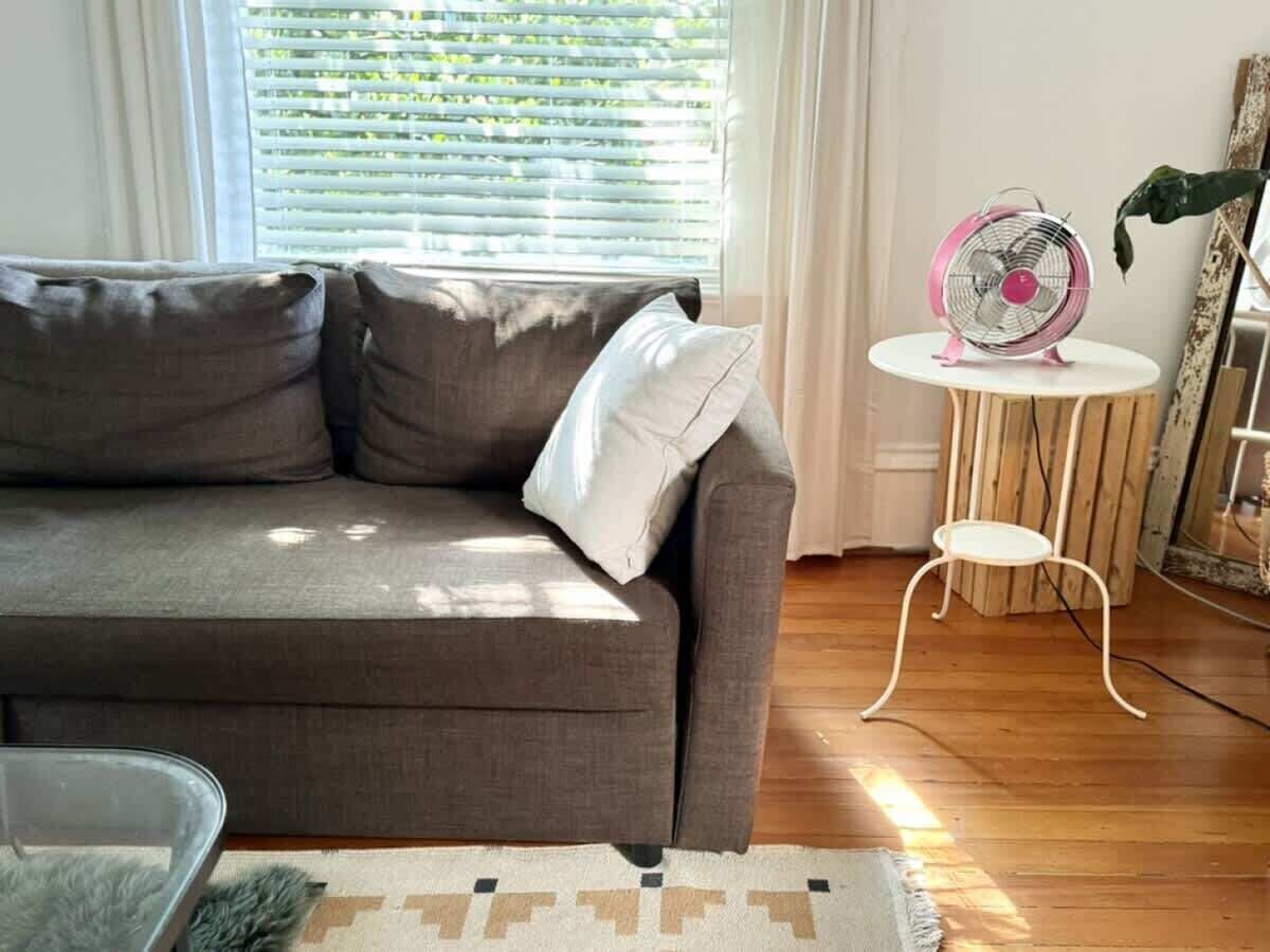 A living room with a grey sofa, a small round table, and a pink fan.