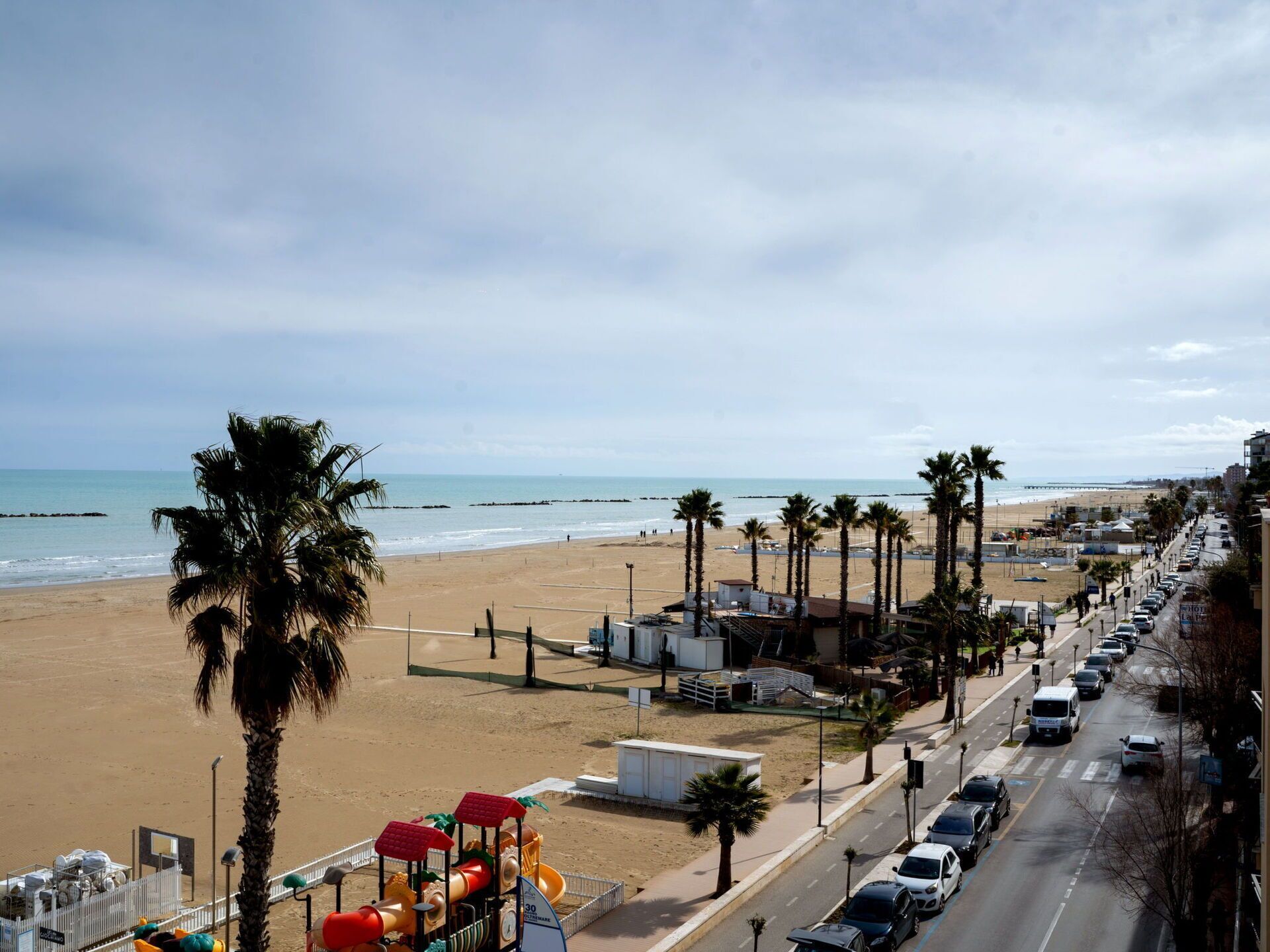 Une route bordée de palmiers, avec des installations de plage, et offrant une vue sur l’océan.
