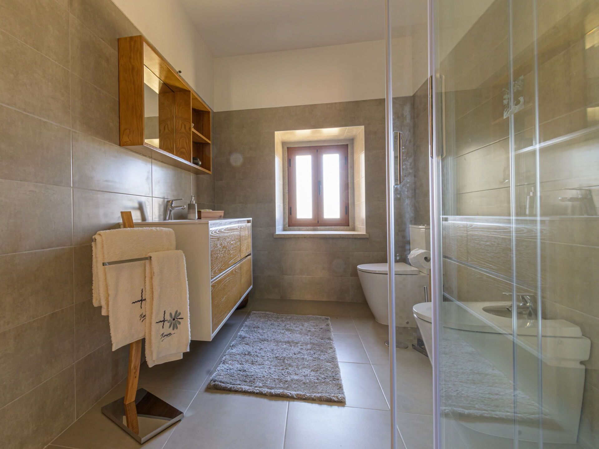 A modern bathroom with a glass shower enclosure, a built-in sink with a wooden vanity, and a toilet.