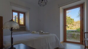 Quarto com cama, escrivaninha com abajur, janela e porta para uma varanda.