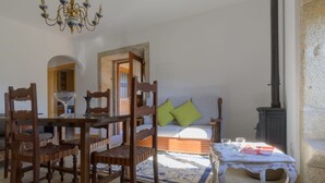 Um quarto aconchegante com uma mesa de jantar, cadeiras, um sofá com almofadas verdes, uma mesinha com copos e um livro, e um fogão antigo.