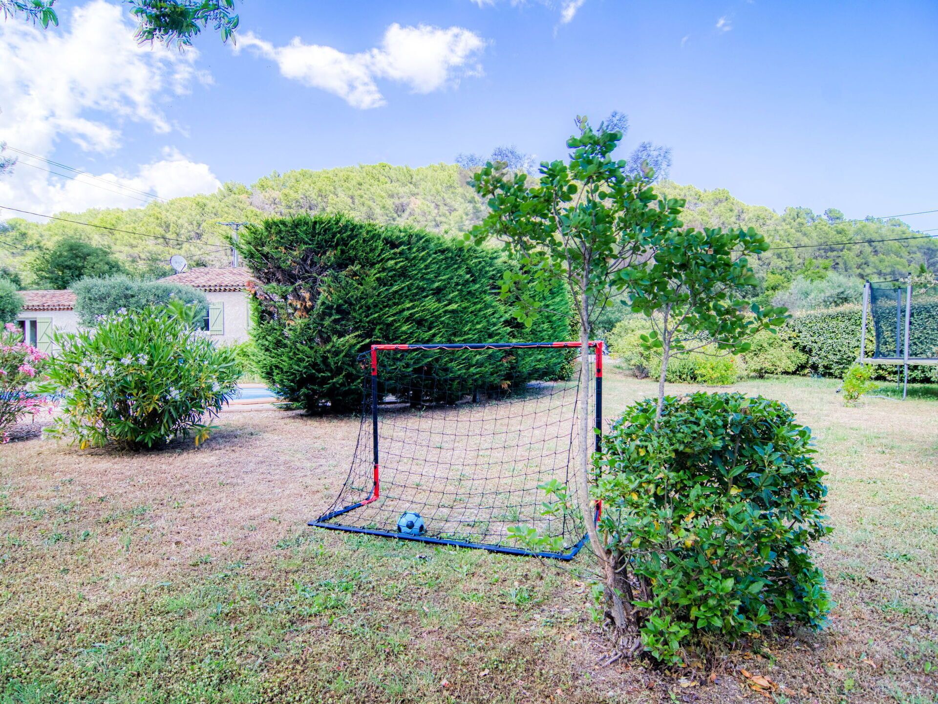 Un arco de fútbol en un área cubierta de césped, con una casa y árboles al fondo.